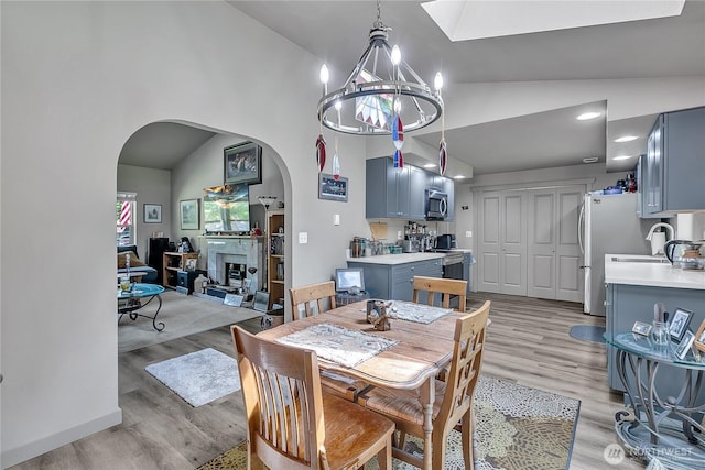 56065608 76th Street Ct E, Puyallup, WA 98371 - dining space with arched walkways, a chandelier, light wood-style floors, high vaulted ceiling, and a glass covered fireplace