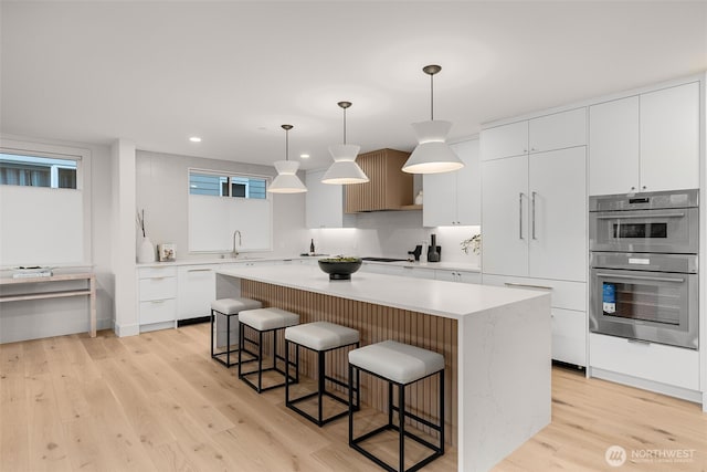 238 4th Ave Unit 101, Kirkland, WA 98033 - kitchen with double oven, a breakfast bar, a kitchen island, light wood finished floors, and recessed lighting