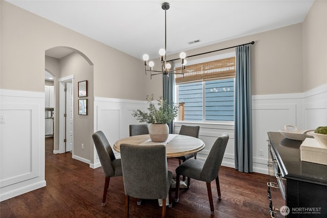 11226 Borgen Loop, Gig Harbor, WA 98332 - dining room with a chandelier, arched walkways, wainscoting, a decorative wall, and dark wood-style flooring