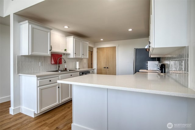 1472 Storm King Ave SW Unit A, Ocean Shores, WA 98569 - kitchen featuring a sink, light wood-style flooring, white cabinets, tasteful backsplash, and a peninsula
