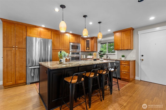 315 10th Ave S Unit 101, Kirkland, WA 98033 - kitchen with stainless steel appliances, brown cabinets, light wood-style flooring, light stone counters, and a center island