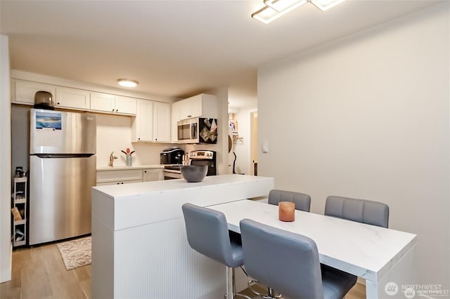 3834 175th Ave NE Unit G16, Redmond, WA 98052 - kitchen with appliances with stainless steel finishes, light wood-type flooring, white cabinets, light countertops, and a breakfast bar area