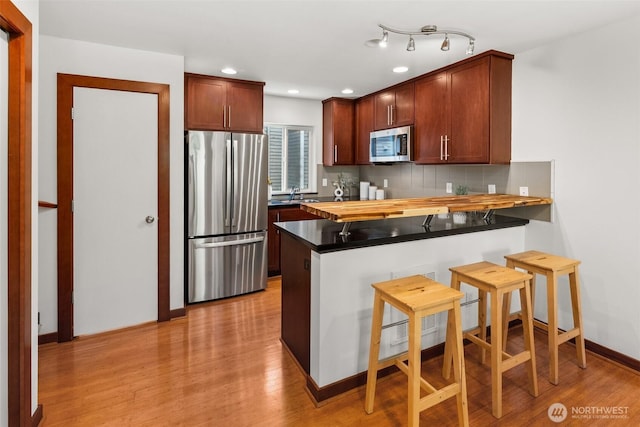 672 NE 40th St, Seattle, WA 98105 - kitchen with appliances with stainless steel finishes, a peninsula, a sink, light wood-type flooring, and tasteful backsplash