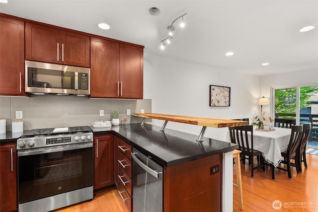 672 NE 40th St, Seattle, WA 98105 - kitchen with stainless steel appliances, a peninsula, dark countertops, light wood finished floors, and recessed lighting