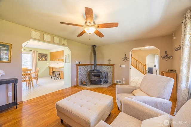 1160 Cays Rd, Sequim, WA 98382 - living room featuring arched walkways, light wood-style floors, ceiling fan, a wood stove, and stairs