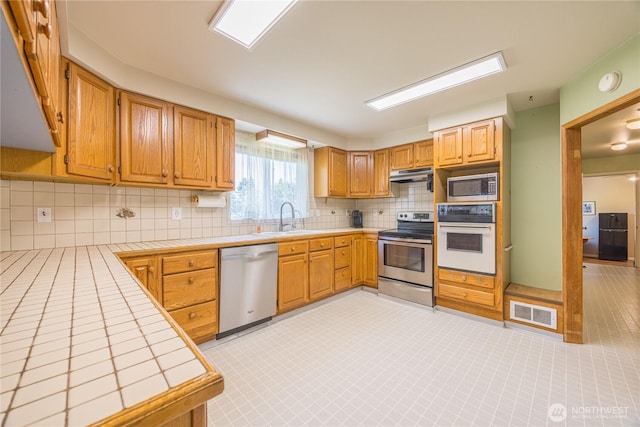 1160 Cays Rd, Sequim, WA 98382 - kitchen featuring appliances with stainless steel finishes, under cabinet range hood, tile countertops, a sink, and backsplash