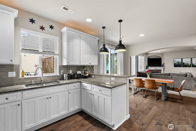 4415 Goldcrest Dr NW, Olympia, WA 98502 - kitchen featuring a sink, a peninsula, arched walkways, white cabinetry, and tasteful backsplash