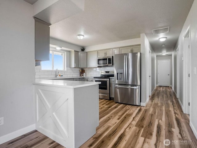 13576 NE Rd 10, Moses Lake, WA 98837 - kitchen with appliances with stainless steel finishes, a peninsula, a textured ceiling, baseboards, and backsplash