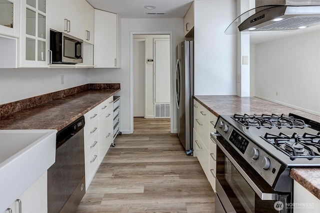 19055 SE 269th St, Covington, WA 98042 - kitchen featuring appliances with stainless steel finishes, extractor fan, dark countertops, glass insert cabinets, and light wood-type flooring