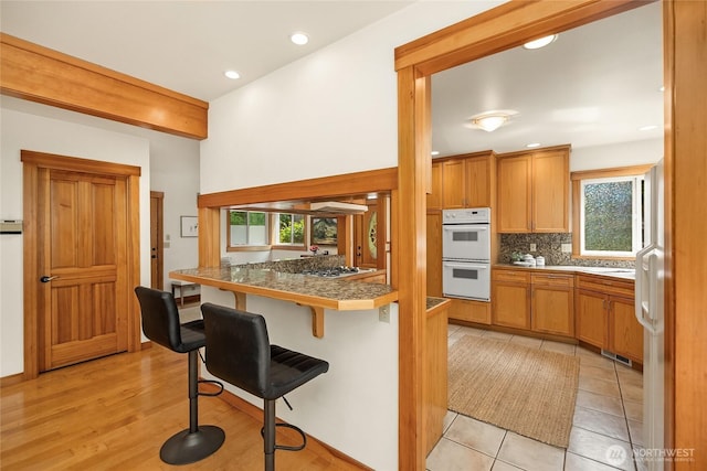 14427 Silven Ave NE, Bainbridge Island, WA 98110 - kitchen with white appliances, a kitchen bar, tasteful backsplash, brown cabinets, and recessed lighting