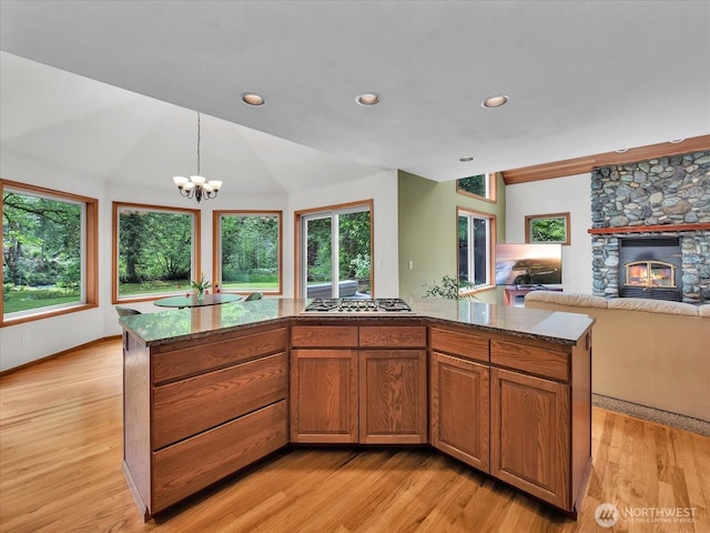 44611 SE 72nd St, Snoqualmie, WA 98065 - kitchen with stainless steel gas stovetop, a fireplace, light wood finished floors, vaulted ceiling, and dark stone countertops