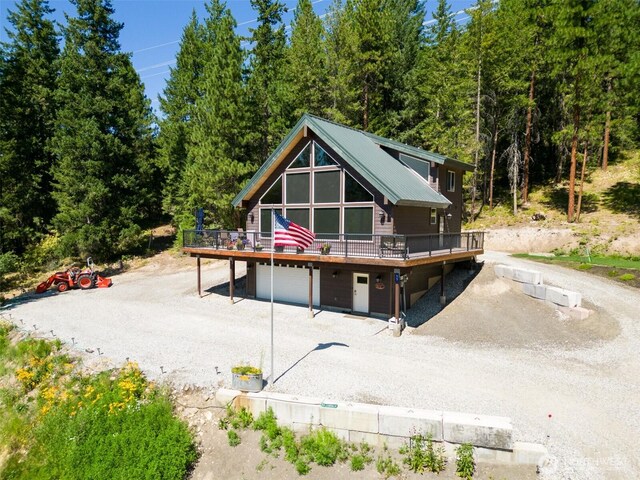 55 Wrangler Ln, Leavenworth, WA 98826 - rear view of house with a wooden deck, dirt driveway, an attached garage, and a view of trees