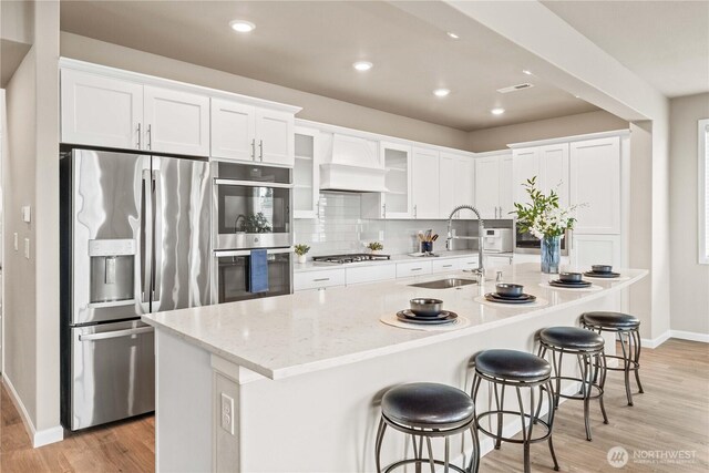 25701 204th Pl SE, Covington, WA 98042 - kitchen with stainless steel appliances, baseboards, light wood-style floors, premium range hood, and white cabinets