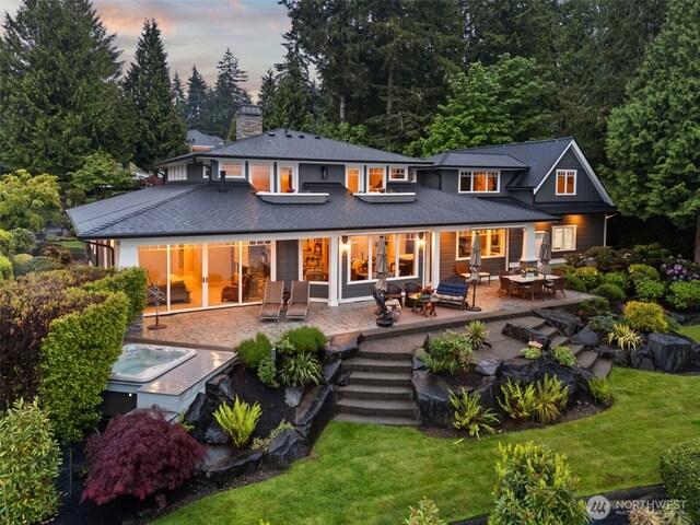 4825 Bayshore Ln NW, Olympia, WA 98502 - back of property at dusk featuring a lawn, an outdoor hot tub, a chimney, a patio area, and roof with shingles