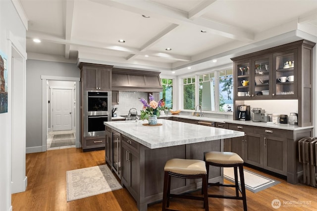 4825 Bayshore Ln NW, Olympia, WA 98502 - kitchen featuring double oven, coffered ceiling, dark brown cabinets, backsplash, and a center island with sink