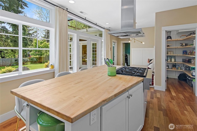 301 Weaver Rd NW, Bainbridge Island, WA 98110 - kitchen with island range hood, butcher block counters, wood finished floors, and white cabinetry