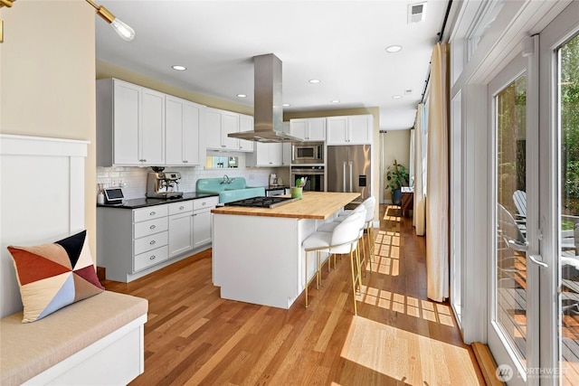 301 Weaver Rd NW, Bainbridge Island, WA 98110 - kitchen featuring island range hood, appliances with stainless steel finishes, wooden counters, light wood finished floors, and white cabinets