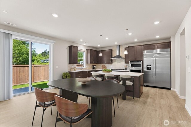 10532 135th Ave NE Unit 32, Kirkland, WA 98033 - kitchen with appliances with stainless steel finishes, wall chimney exhaust hood, dark brown cabinets, light wood-type flooring, and backsplash