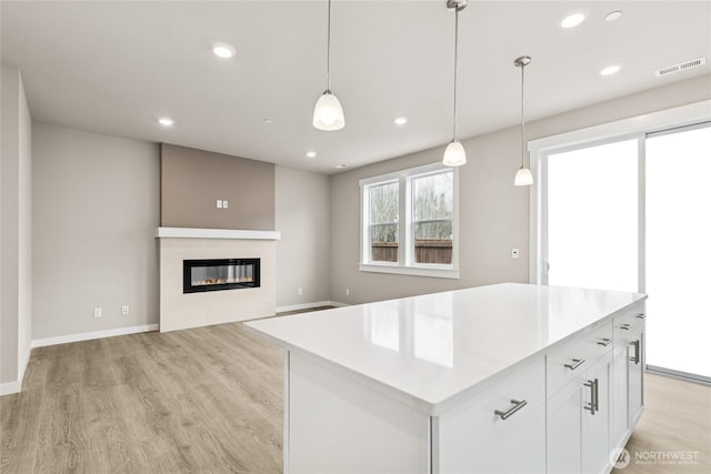 13473 NE 105th Ct Unit 12, Kirkland, WA 98033 - kitchen featuring light wood-style flooring, a glass covered fireplace, white cabinetry, pendant lighting, and light countertops