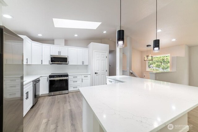 8302 319th St NW, Stanwood, WA 98292 - kitchen featuring stainless steel appliances, light wood-style floors, a skylight, decorative backsplash, and lofted ceiling