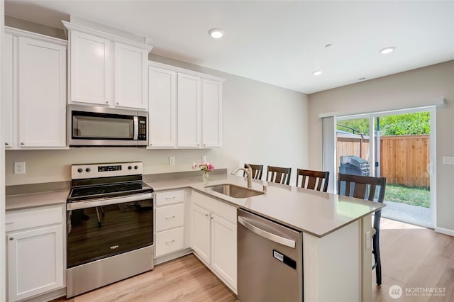 8605 E Gilman Ave, Arlington, WA 98223 - kitchen with appliances with stainless steel finishes, a peninsula, light wood finished floors, a breakfast bar area, and white cabinetry