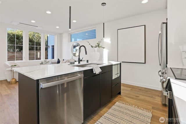 8757B Palatine Ave N, Seattle, WA 98103 - kitchen featuring appliances with stainless steel finishes, dark cabinets, a center island with sink, a sink, and light wood-style flooring