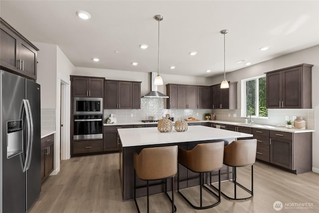 769 SE 12th Pl Unit 29, North Bend, WA 98045 - kitchen featuring stainless steel appliances, wall chimney exhaust hood, dark brown cabinetry, a sink, and light wood finished floors