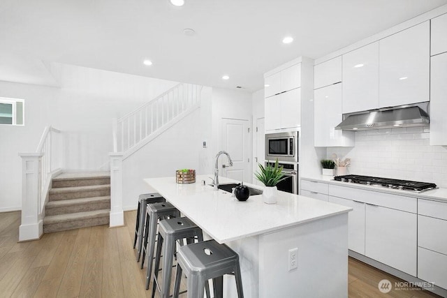 14144 270th Ln NE, Duvall, WA 98019 - kitchen with wall chimney exhaust hood, appliances with stainless steel finishes, a breakfast bar area, white cabinetry, and tasteful backsplash