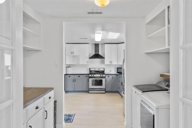 7715 236th St SW, Edmonds, WA 98026 - kitchen with open shelves, stainless steel gas range oven, wall chimney range hood, washer and clothes dryer, and light wood-style floors