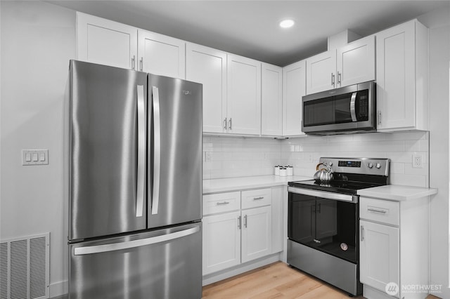 3514 S Tyler St, Tacoma, WA 98409 - kitchen with appliances with stainless steel finishes, light countertops, white cabinets, light wood-style flooring, and tasteful backsplash