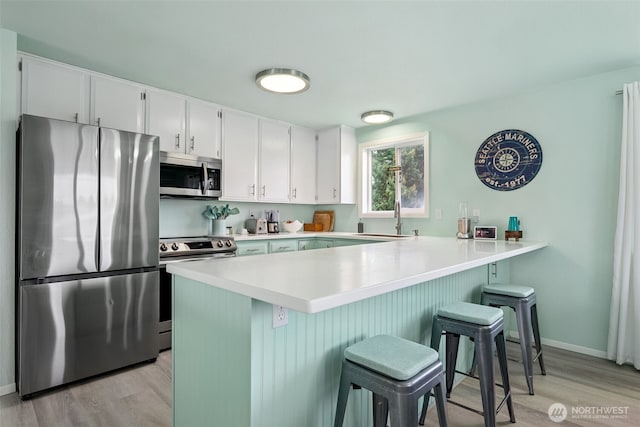 177 N Razor Clam Dr SW, Ocean Shores, WA 98569 - kitchen with stainless steel appliances, a peninsula, light wood-style floors, a sink, and a breakfast bar