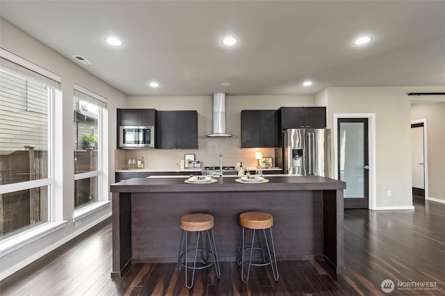 5614 Douglas Ave SE, Auburn, WA 98092 - kitchen with wall chimney range hood, stainless steel appliances, a breakfast bar area, tasteful backsplash, and an island with sink