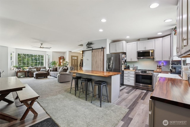 822 Filbert Rd, Cle Elum, WA 98922 - kitchen featuring butcher block counters, appliances with stainless steel finishes, a barn door, a breakfast bar area, and backsplash