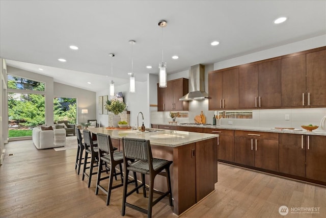 12126NE 106th Pl, Kirkland, WA 98033 - kitchen featuring wall chimney exhaust hood, a sink, decorative backsplash, light wood finished floors, and a breakfast bar area