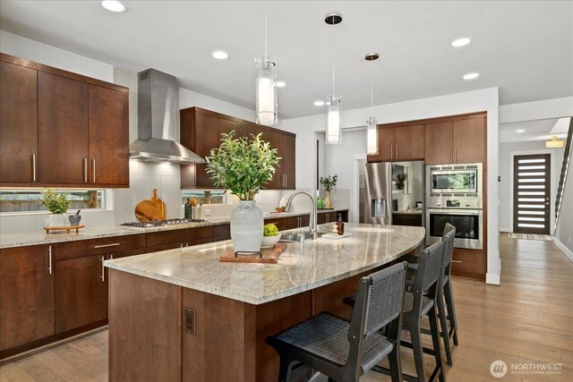 12126NE 106th Pl, Kirkland, WA 98033 - kitchen featuring appliances with stainless steel finishes, wall chimney range hood, a breakfast bar, recessed lighting, and light wood-style flooring