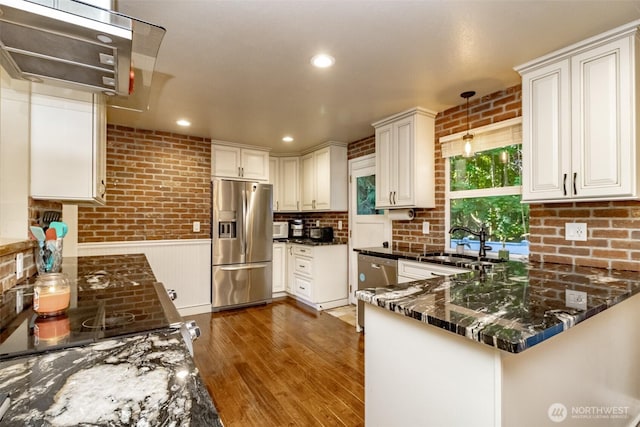 10908 151st St E, Puyallup, WA 98374 - kitchen with stainless steel appliances, wood finished floors, brick wall, a peninsula, and hanging light fixtures