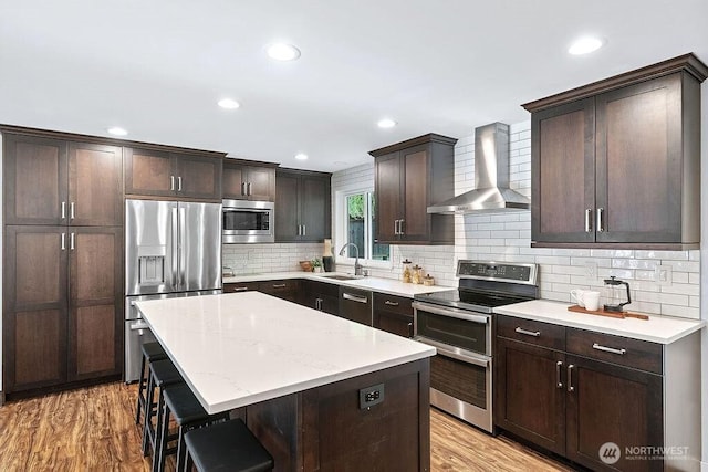 14520 78th Ave NE, Kenmore, WA 98028 - kitchen featuring wall chimney exhaust hood, stainless steel appliances, a kitchen breakfast bar, dark brown cabinets, and light wood-style floors