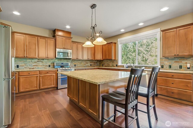 9440 Piperhill Dr SE, Olympia, WA 98513 - kitchen with appliances with stainless steel finishes, decorative backsplash, dark wood-style floors, a kitchen breakfast bar, and a kitchen island
