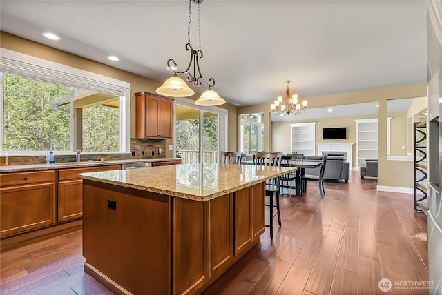 9440 Piperhill Dr SE, Olympia, WA 98513 - kitchen featuring brown cabinetry, a kitchen island, light stone counters, a chandelier, and pendant lighting