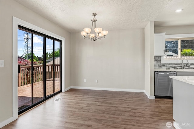 6015 NW Perthshire Rd, Vancouver, WA 98663 - unfurnished dining area with wood finished floors, a chandelier, a textured ceiling, a sink, and baseboards