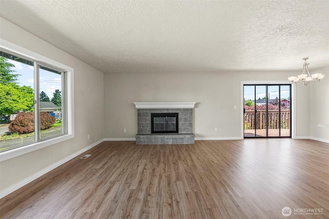 6015 NW Perthshire Rd, Vancouver, WA 98663 - unfurnished living room featuring a textured ceiling, wood finished floors, a chandelier, a stone fireplace, and baseboards