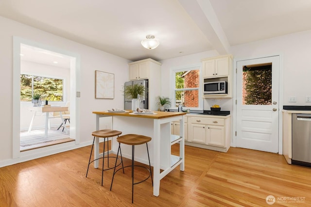 1214 NE 98th St, Seattle, WA 98115 - kitchen featuring appliances with stainless steel finishes, white cabinetry, light wood-style floors, a kitchen bar, and a kitchen island