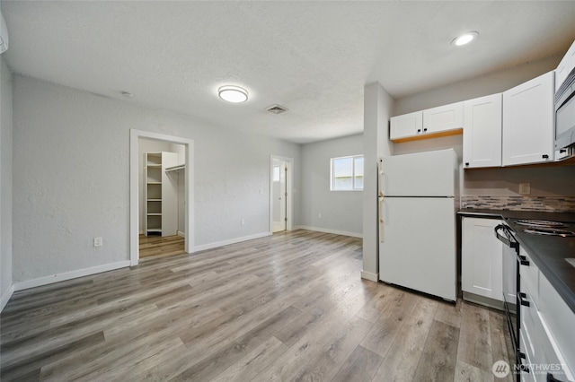 1128 W Elm St, Walla Walla, WA 99362 - kitchen with freestanding refrigerator, dark countertops, white cabinets, light wood-type flooring, and baseboards
