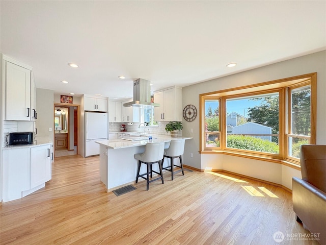 22 E Bedinger Rd, Sequim, WA 98382 - kitchen with freestanding refrigerator, black microwave, island exhaust hood, a peninsula, and light wood-style flooring