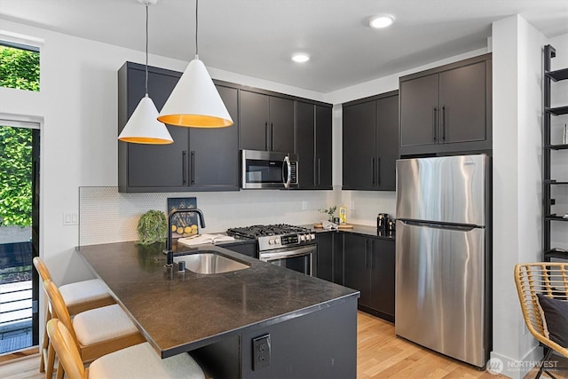 1134 32nd Ave E Unit B, Seattle, WA 98112 - kitchen with appliances with stainless steel finishes, a peninsula, a sink, dark cabinets, and light wood-type flooring