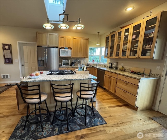 851 Heichel Rd, Camano Island, WA 98282 - kitchen featuring appliances with stainless steel finishes, a kitchen island, light wood-style floors, a kitchen bar, and glass insert cabinets