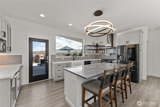 1425 Appleridge St, Wenatchee, WA 98801 - kitchen featuring wall chimney exhaust hood, appliances with stainless steel finishes, a chandelier, tasteful backsplash, and light wood finished floors
