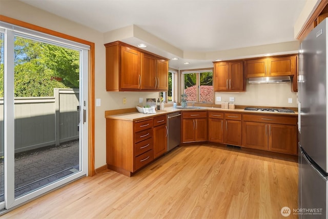 1211 6th Pl S, Edmonds, WA 98020 - kitchen featuring appliances with stainless steel finishes, under cabinet range hood, light wood-style floors, light countertops, and brown cabinetry