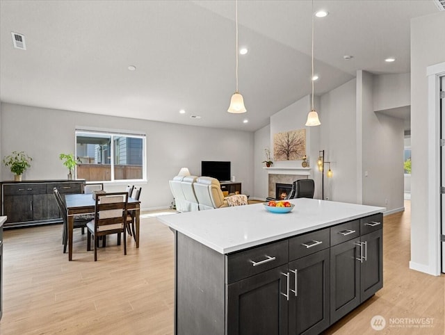 4413 NE 182nd St Unit 111, Vancouver, WA 98686 - kitchen featuring a warm lit fireplace, light countertops, light wood-type flooring, a kitchen island, and hanging light fixtures