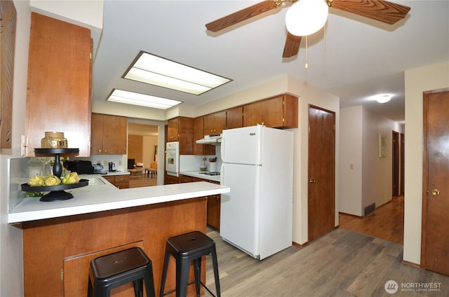 18215 108th Ave NE, Bothell, WA 98011 - kitchen featuring white appliances, under cabinet range hood, wood finished floors, brown cabinets, and light countertops